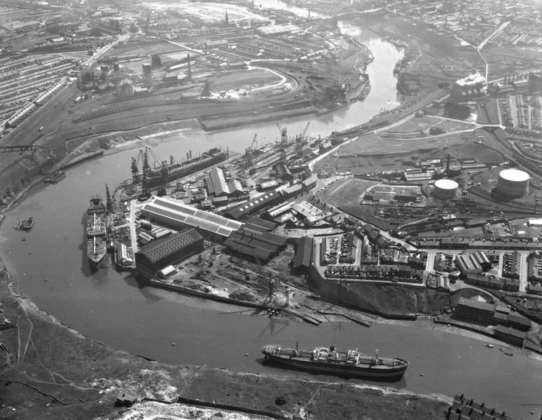 Aerial view of a large shipyard in Sunderland, showing multiple ships in dock, industrial buildings, cranes, and surrounding infrastructure. The river curves through the center, with cranes and shipbuilding equipment scattered along the docks. Industrial plants and tanks are visible nearby.