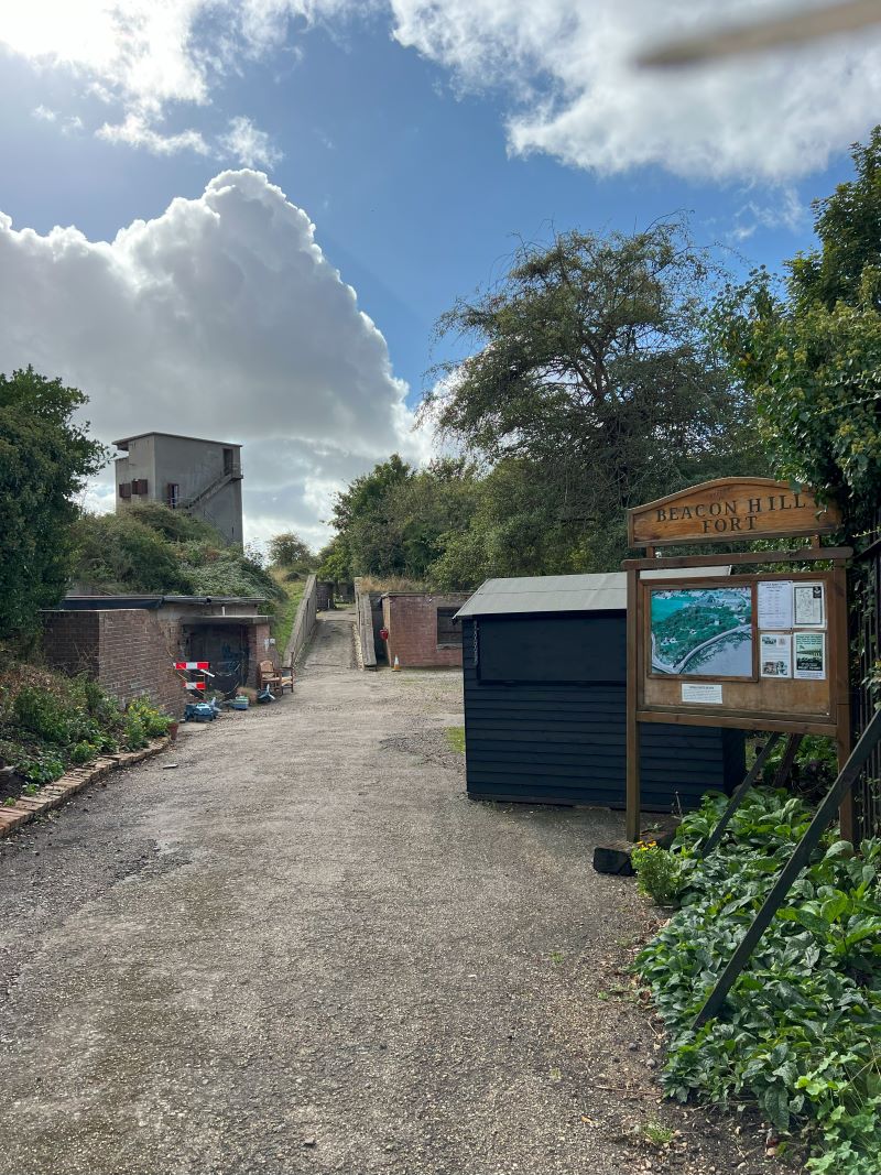 Path leading to Beacon Hill Fort in Harwich, UK, with historical buildings and an information sign on the right