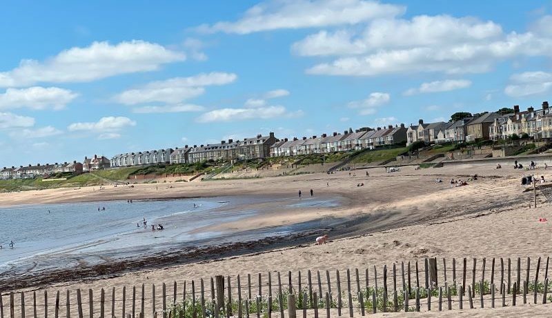 Newbiggin-by-the-Sea beach with sandy shoreline, sea, and houses in the background