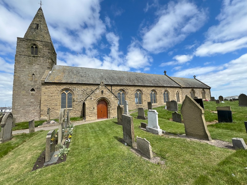 St Bartholomew's Church with graveyard in Newbiggin-by-the-Sea under a blue sky