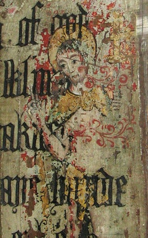 Medieval wall painting uncovered beneath whitewash at Binham Priory, Norfolk, England, depicting a haloed religious figure with decorative Gothic lettering.