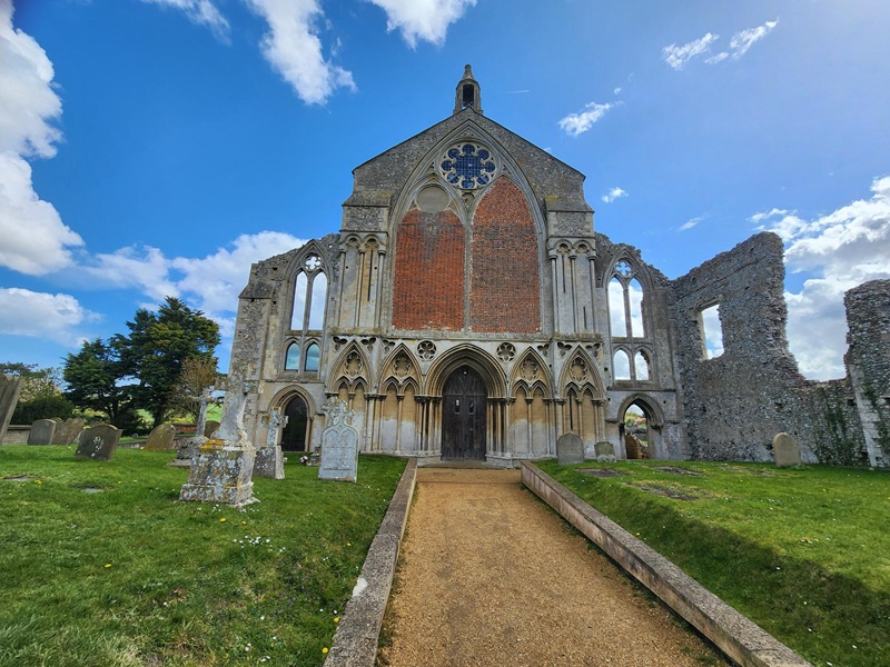 West front of Binham Priory in Norfolk, England, showcasing early Gothic architecture, bar tracery windows, medieval stone carvings, and historic church ruins.