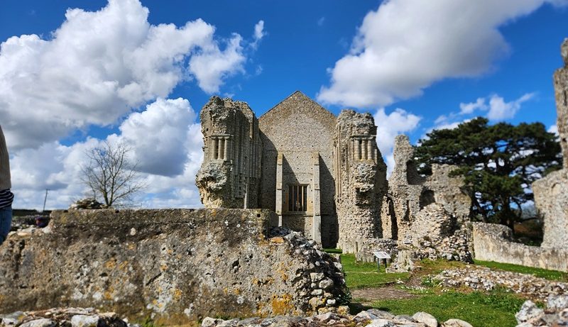 Ruins of Binham Priory in Norfolk, England, featuring medieval stone walls and Gothic architectural remains beneath a dramatic blue sky with towering clouds.