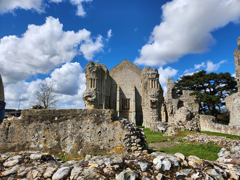 Ruins of Binham Priory in Norfolk, England, featuring medieval stone walls and Gothic architectural remains beneath a dramatic blue sky with towering clouds.