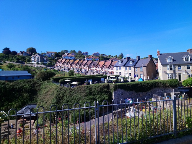 View of pastel-coloured houses on the hillside overlooking Beer village in Devon, England, under a clear blue sky.