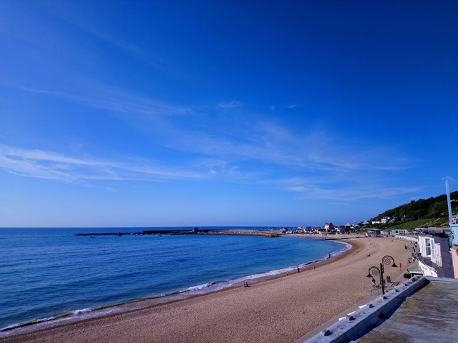 Panoramic view of Lyme Regis Beach and the Cobb Harbour on Dorset's Jurassic Coast under a clear blue sky.