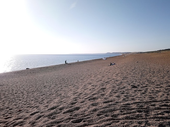 West Bexington Beach on the Jurassic Coast with a wide shingle shoreline, calm sea, and clear blue sky.
